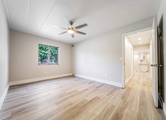 A room with a ceiling fan and a window with a view of trees.