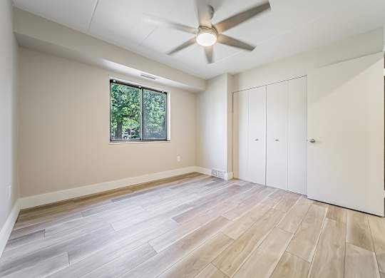 A room with a ceiling fan and a window with a view of trees.