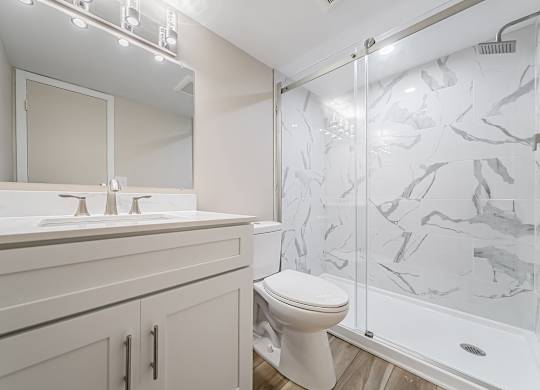 A white toilet sits in a bathroom with a marble shower wall.