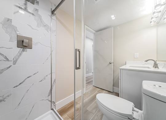 A bathroom with a marble tile shower and a white toilet.