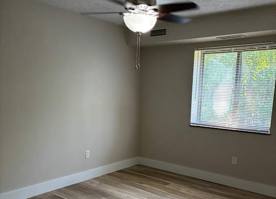 A room with a ceiling fan and a window with blinds.