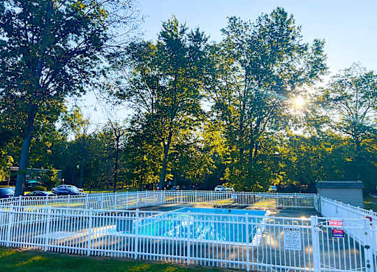 A pool surrounded by a white fence with trees in the background.