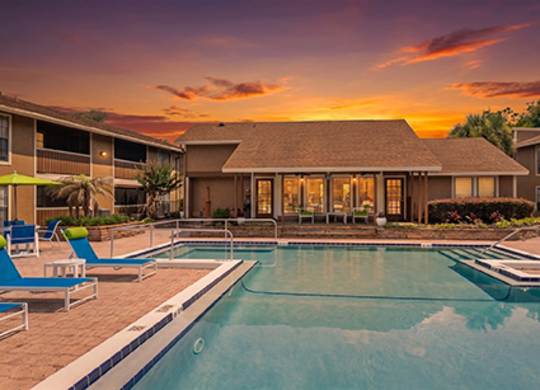 A swimming pool in front of a house with a sunset in the background.