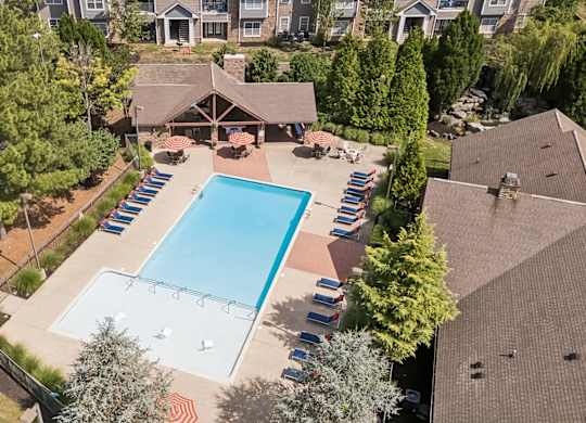 An aerial view of a swimming pool surrounded by trees and a parking lot.