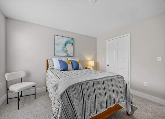 A bedroom with a bed, chair, and painting.