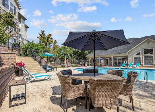 A patio with a table and chairs and a pool in the background.