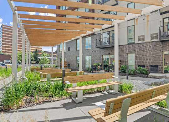 A wooden bench with a green armrest is in the foreground of a modern outdoor seating area.