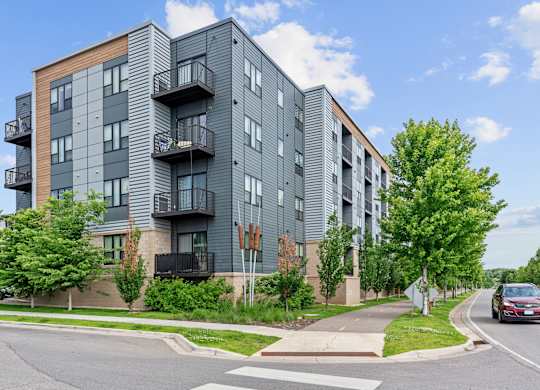 A modern apartment building with balconies and a car on the street.