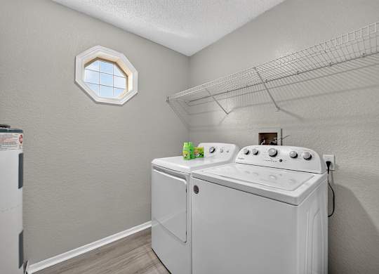 A white washing machine in a laundry room with a window above it.