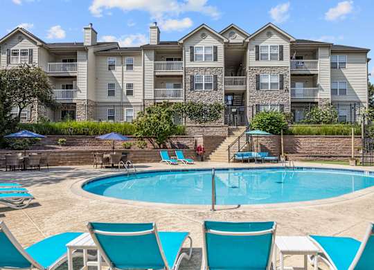 A large apartment complex with a pool and lounge chairs.