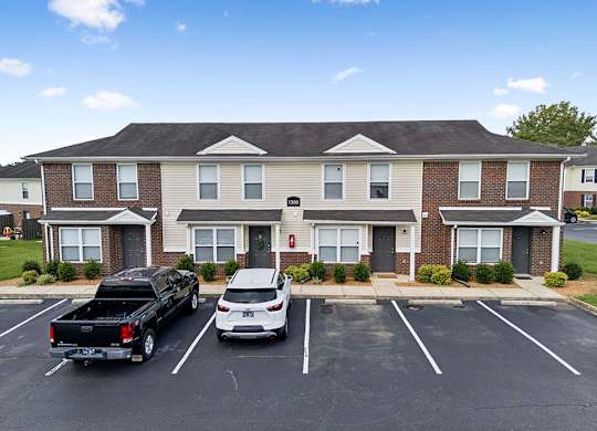 Two cars are parked in a parking lot in front of a brick apartment building.