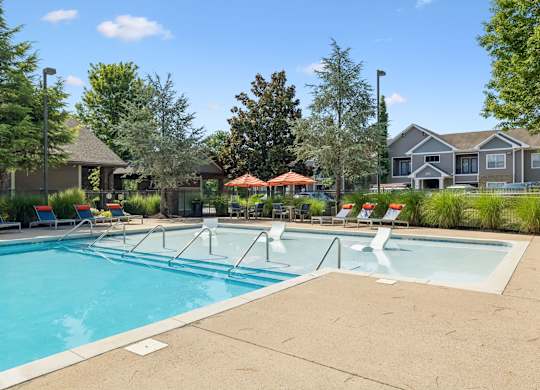 A large swimming pool with a few chairs and umbrellas.