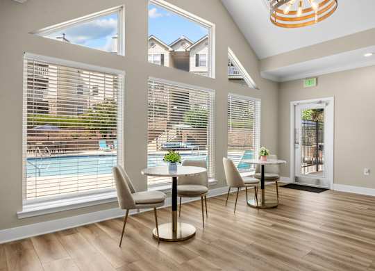 A dining room with a table and chairs and a view of a pool and houses outside the window.