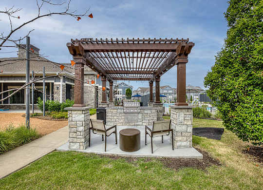 A wooden pergola with a bench and table is in the foreground of a residential area.
