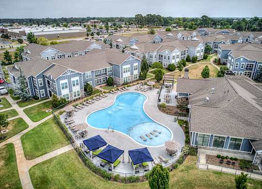 A large swimming pool surrounded by blue umbrellas and lounge chairs in a residential area.