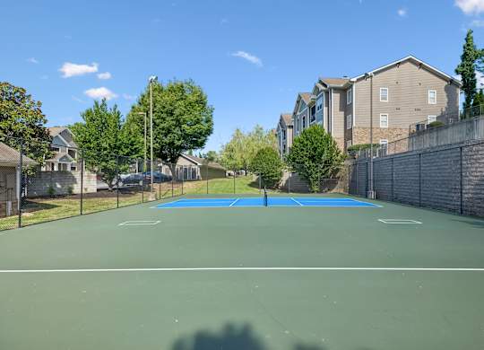 A tennis court surrounded by a fence and apartment buildings.