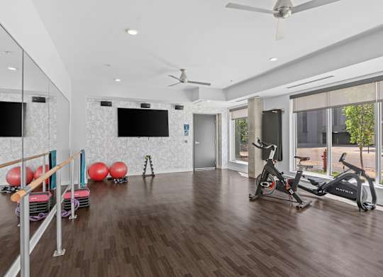 A spacious room with a wooden floor, a mirror, a fan, and exercise equipment.