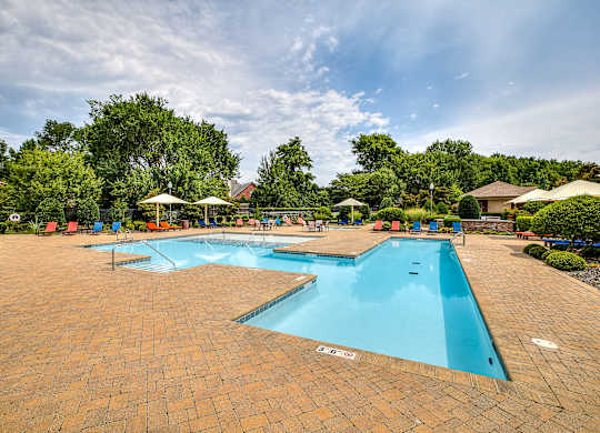 A large outdoor swimming pool surrounded by a brick patio and lounge chairs.