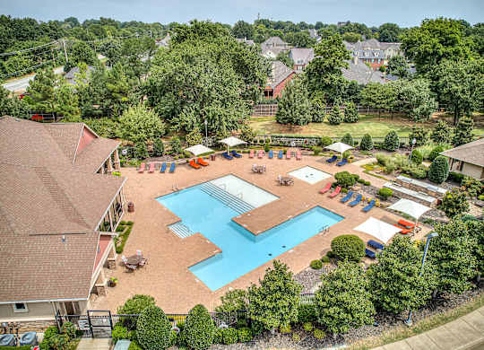 A large swimming pool surrounded by trees and a playground.