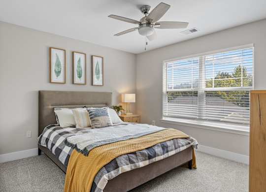 A bedroom with a bed, a ceiling fan, and two framed pictures on the wall.
