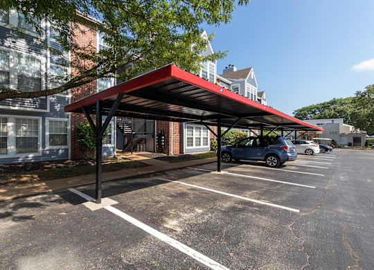 A view of a parking lot near a residence entrance with a red carport canopy over several vehicles.