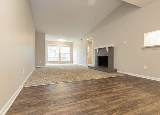 A large living room featuring a fireplace, beige carpeting, bright windows, and a vaulted ceiling.