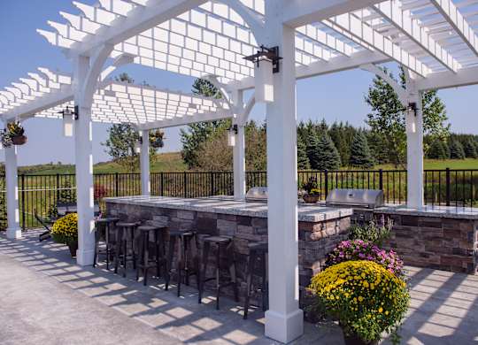 A white pergola with a black fence and a stone wall with a bar under it.