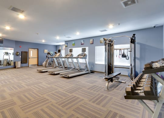 a gym with treadmills and weights and a staircase