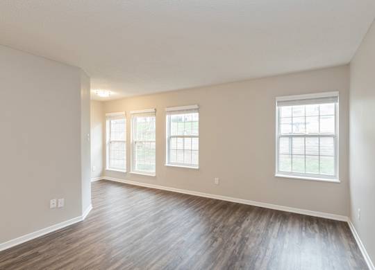 A room with wooden floors and three windows.