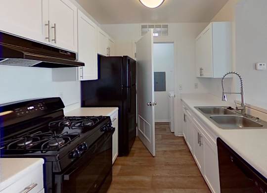 A kitchen with black appliances and white countertops and wood-style floors.