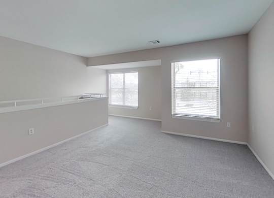 A spacious room with carpeted flooring and two large windows.