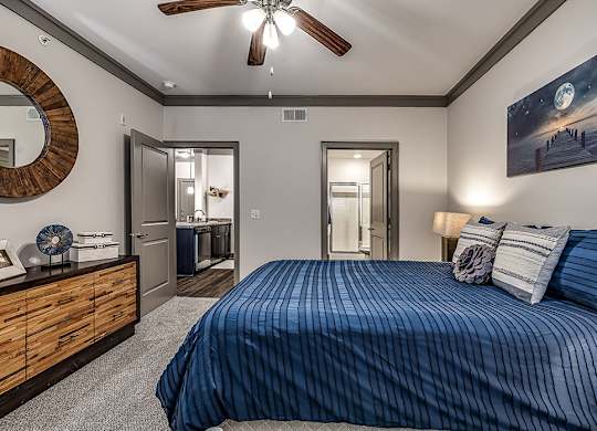A bedroom with a bed, dresser, mirror, and a ceiling fan.