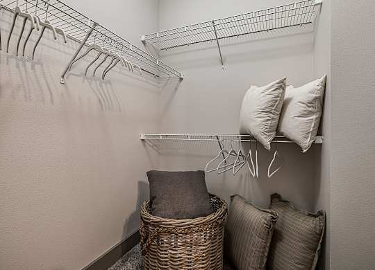 A room with a white wall and a wire shelving unit with clothes hanging on it.