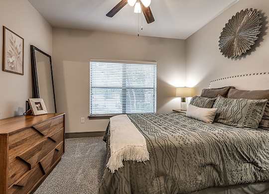 A bedroom with a bed, dresser, and window with blinds.