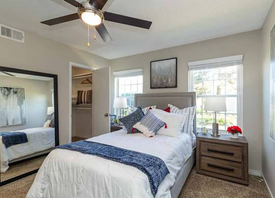A spacious bedroom with a large bed, a ceiling fan, and two windows.