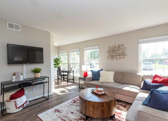 A living room with three windows, a couch, a coffee table, and a television.