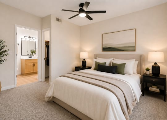 A bedroom with a large bed, a ceiling fan, and a potted plant.