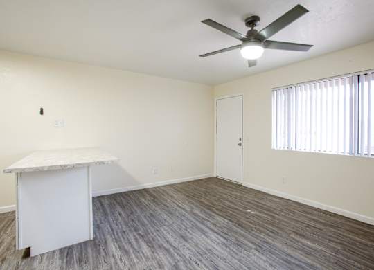A room with a fan, a table, and a window with blinds.