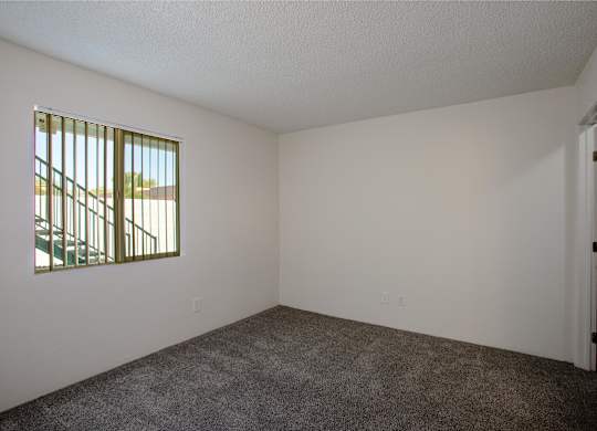 A room with a carpeted floor and a window with bars.