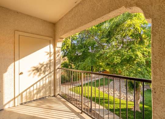 A balcony with a metal railing and a view of a green lawn and trees.