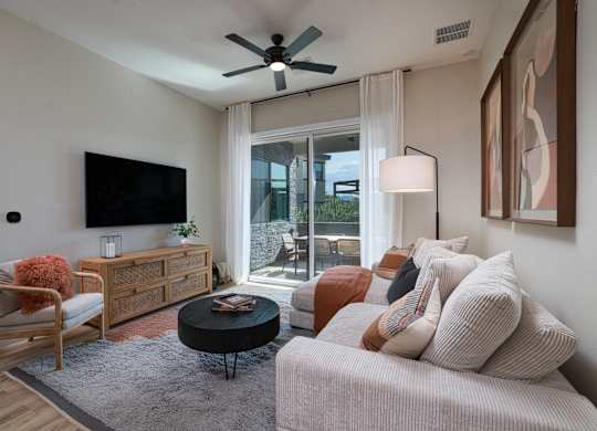 A living room with a white couch, a wooden chair, a black coffee table, and a flat-screen TV mounted on the wall.