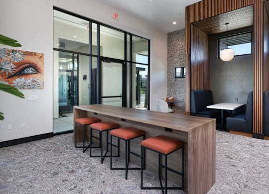 A long wooden table with four chairs with red cushions in front of a glass door.