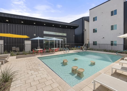 a swimming pool with tables and umbrellas in front of a building at SECOND AVE COMMONS | BRAND-NEW, Mesa