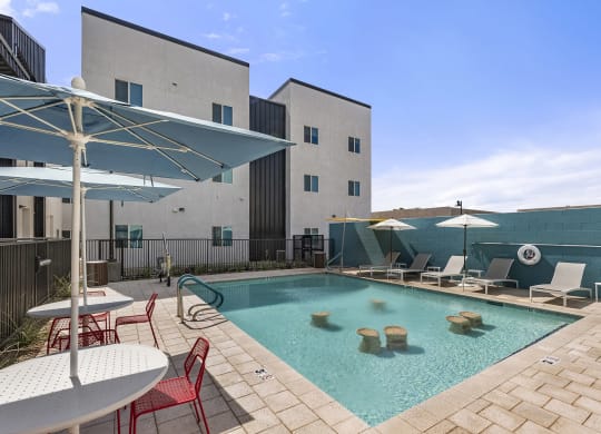 a swimming pool with chairs and umbrellas and a building in the background at SECOND AVE COMMONS | BRAND-NEW, Mesa, Arizona