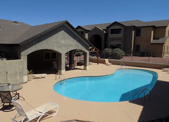 A swimming pool in a backyard with a patio and a house in the background.