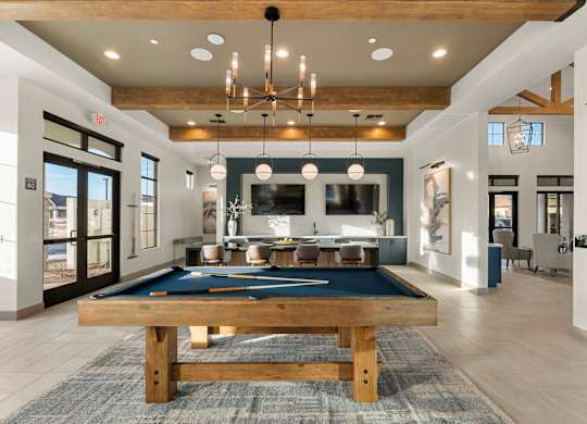A pool table is in the middle of a room with a bar and a dining table.
