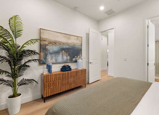 A room with a large painting on the wall and a bench with a potted plant on it.