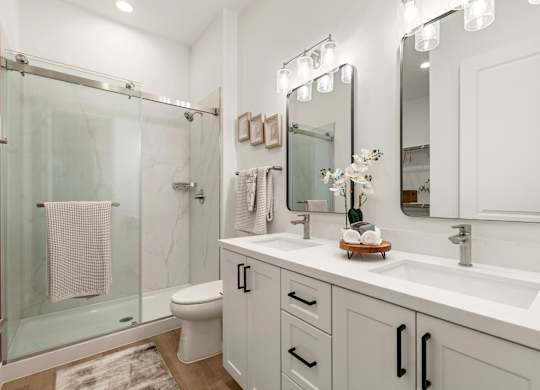 A white bathroom with a glass shower stall and a towel hanging on the glass door.