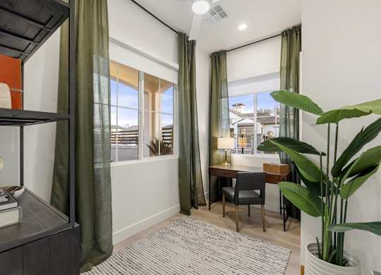 A room with a desk, chair, and a large window with green curtains.
