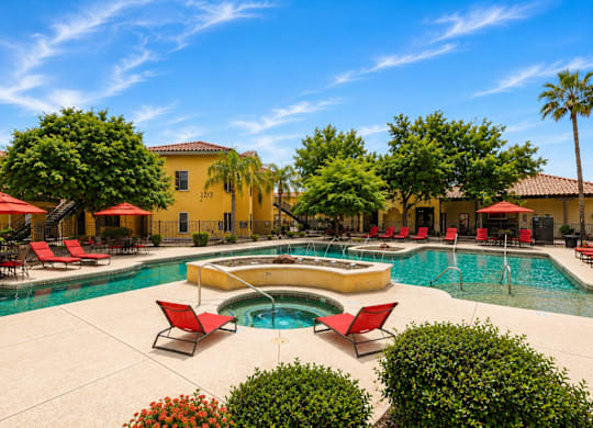 A pool area with red chairs and a yellow building in the background.